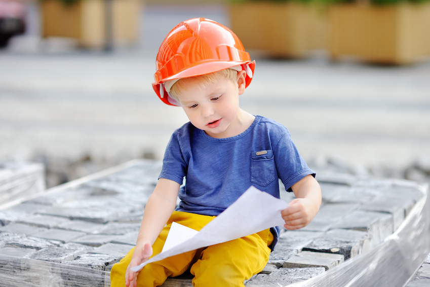 Portrait of little builder in hardhats reading construction drawing. Little boy`s dream concept